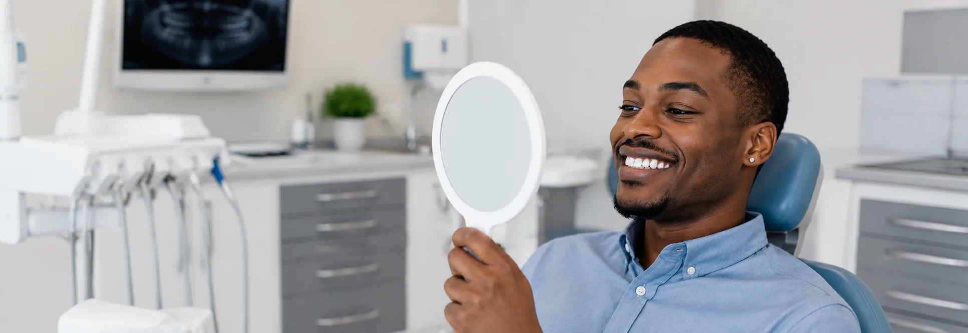Smiling man in a dental chair looking into a hand mirror
